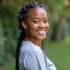 Young woman with braids smiling in a green outdoor setting.